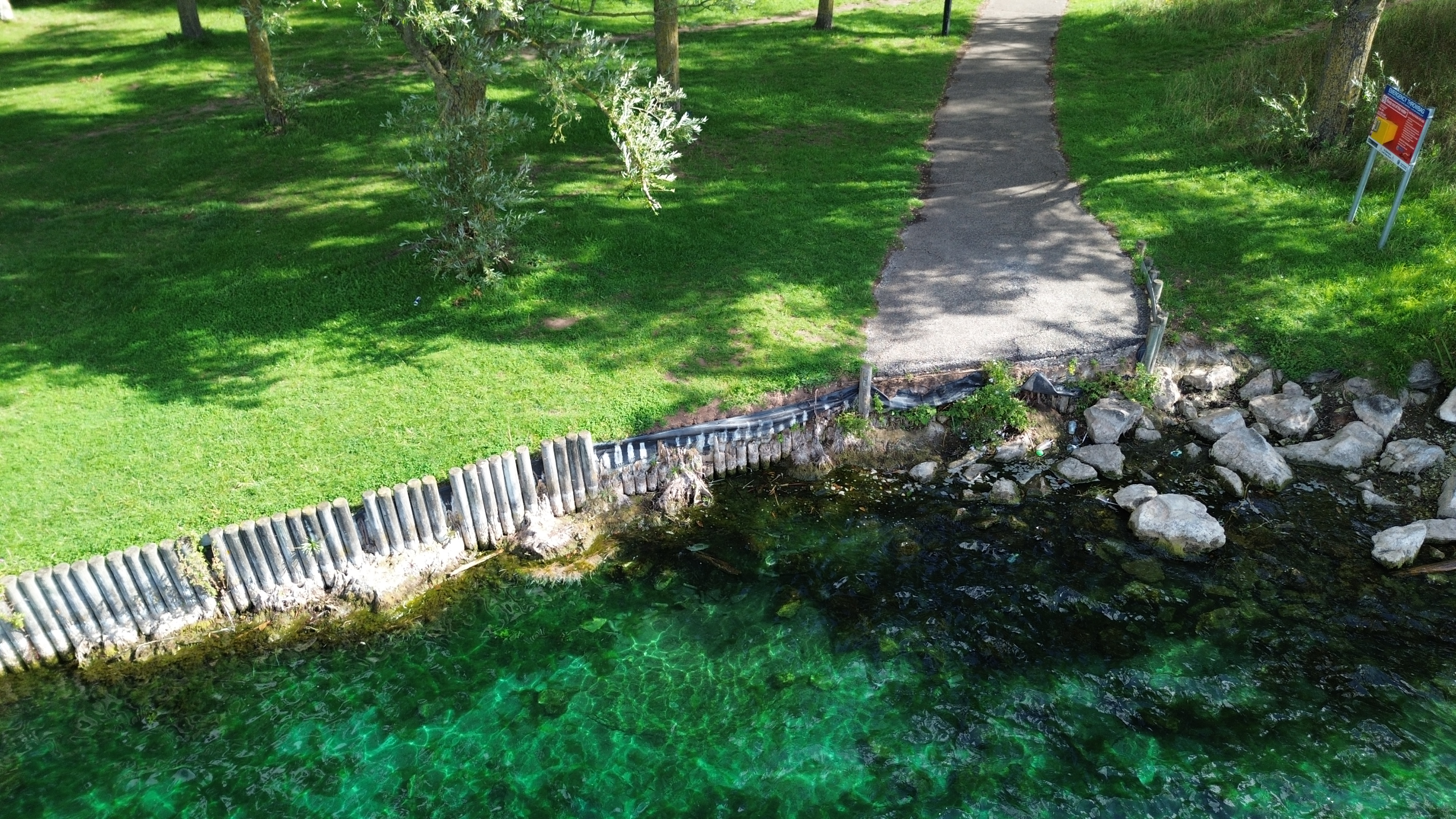 Path edge and rock shoreline. The concrete path meets the collapsed timber wall beside the shoreline rocks.